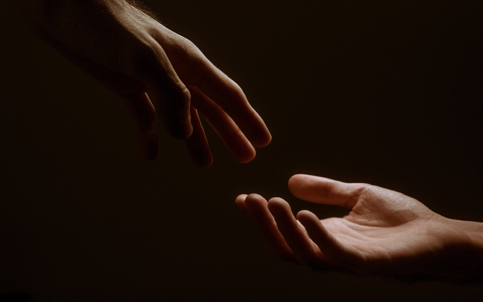 Two hands reaching towards each other on a black background